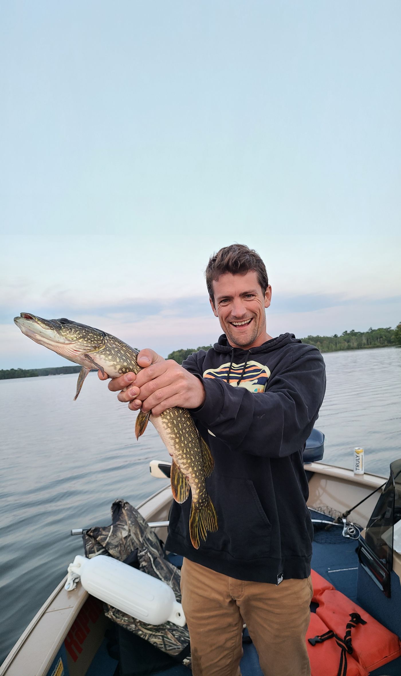 Holding up a northern pike caught from a boat on a lake at sunset