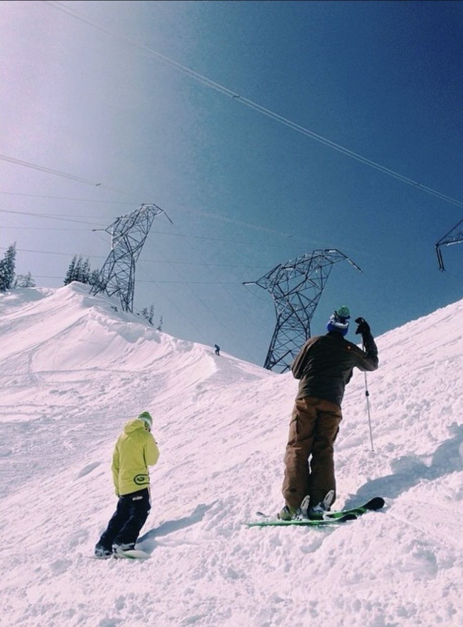 Two snowboarders looking out over a snowy run with transmission towers in the distance