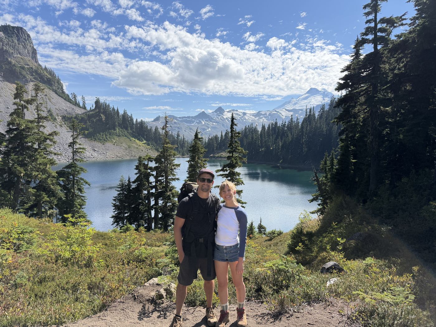 A couple standing above an alpine lake with snow-capped peaks in the background