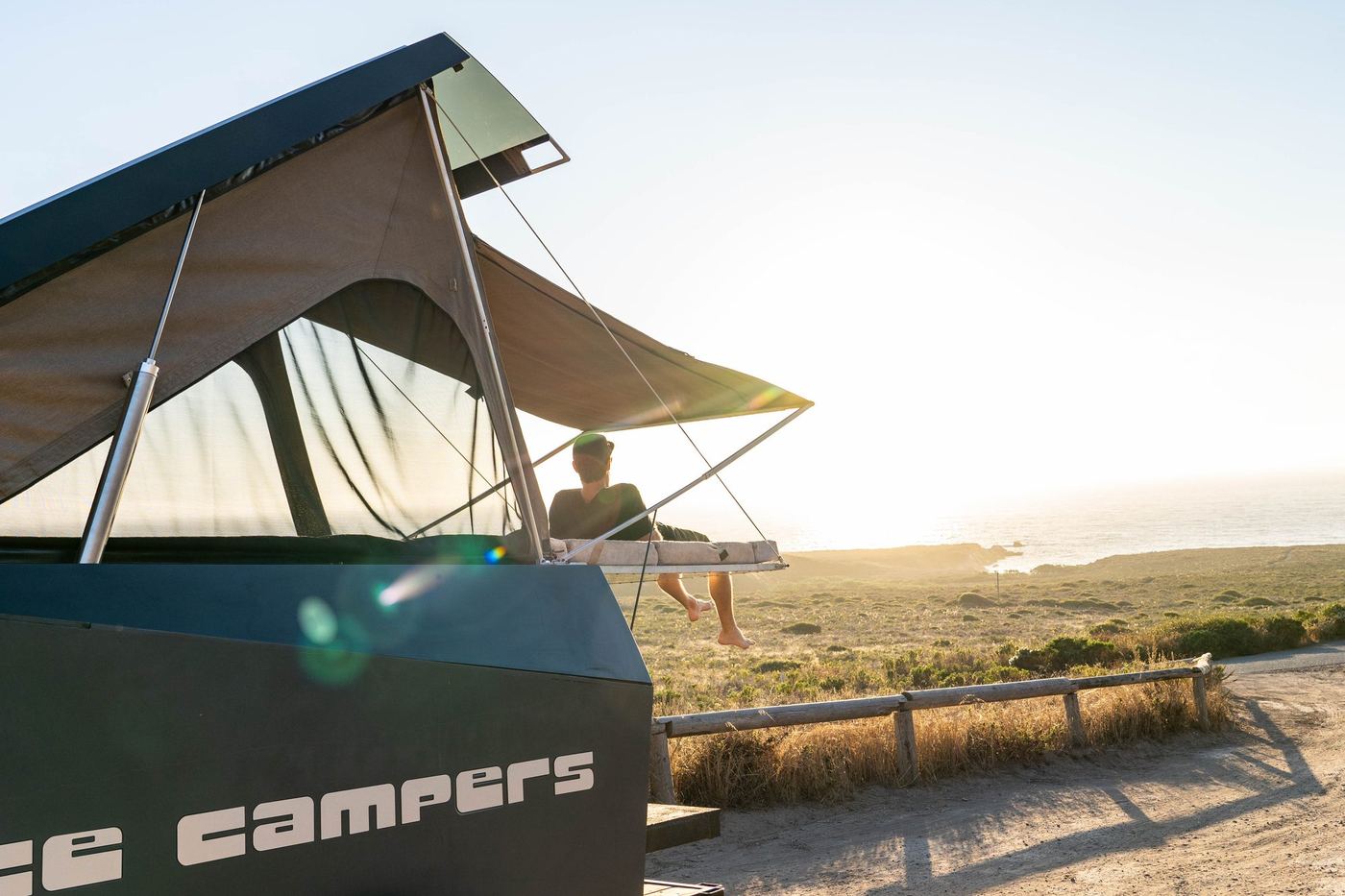 Lee sitting in the open rooftop tent of a Space Campers camper at sunset, overlooking the California coast