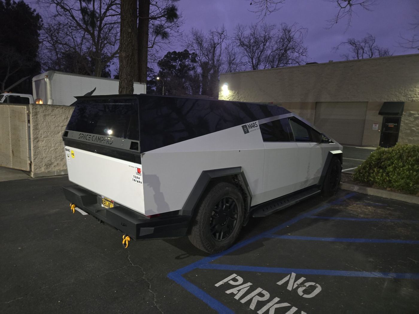 A white Cybertruck with a color-matched cap at night, Space Campers lettering across the hatch