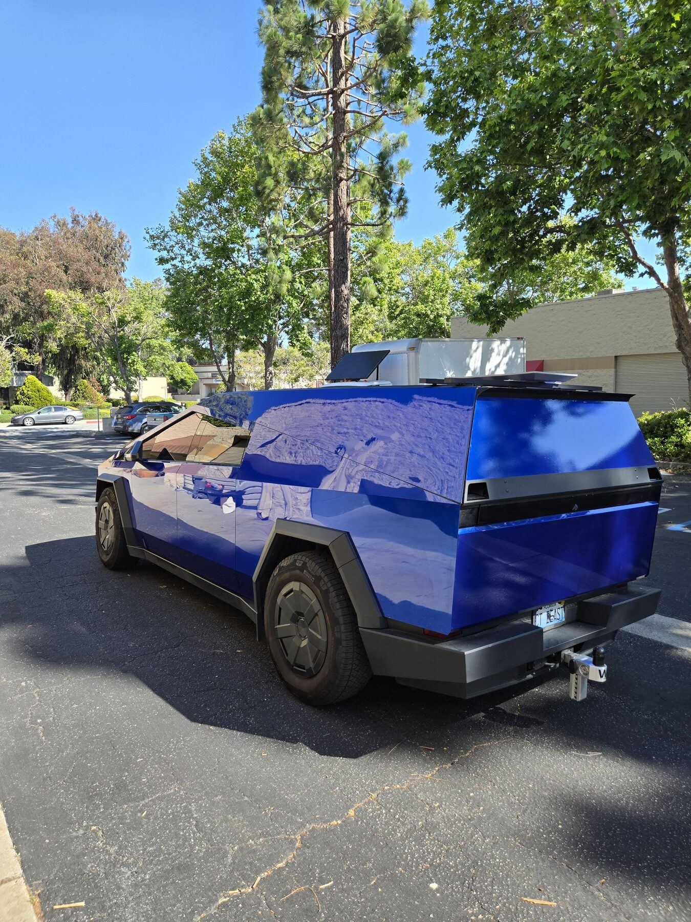 A cobalt blue chrome-wrapped Cybertruck with a matching blue cap and roof-mounted solar panels