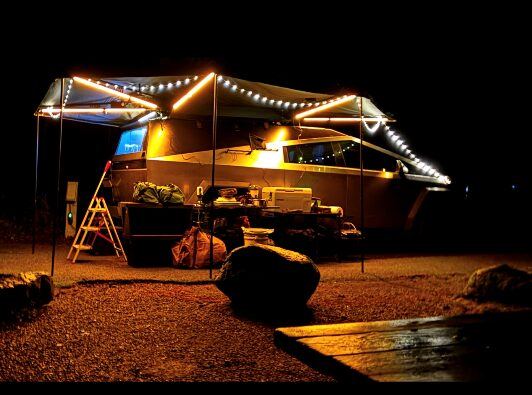 The camp lit up at night, awning extended and string lights running along the truck