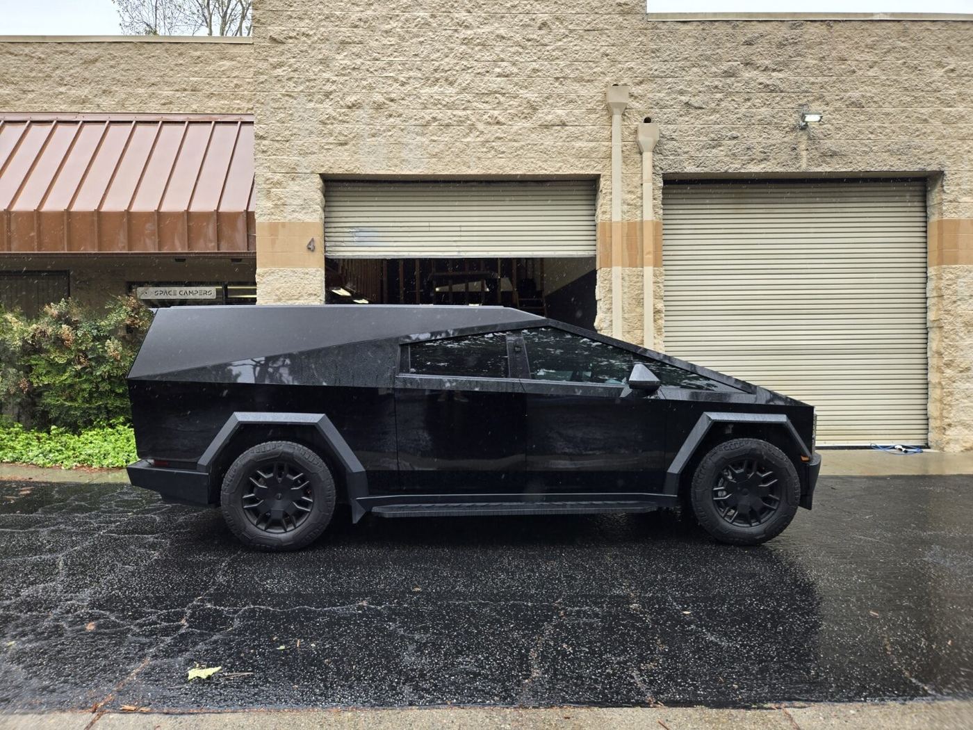 Side profile of a gloss black Cybertruck and cap parked outside the Space Campers unit in the rain