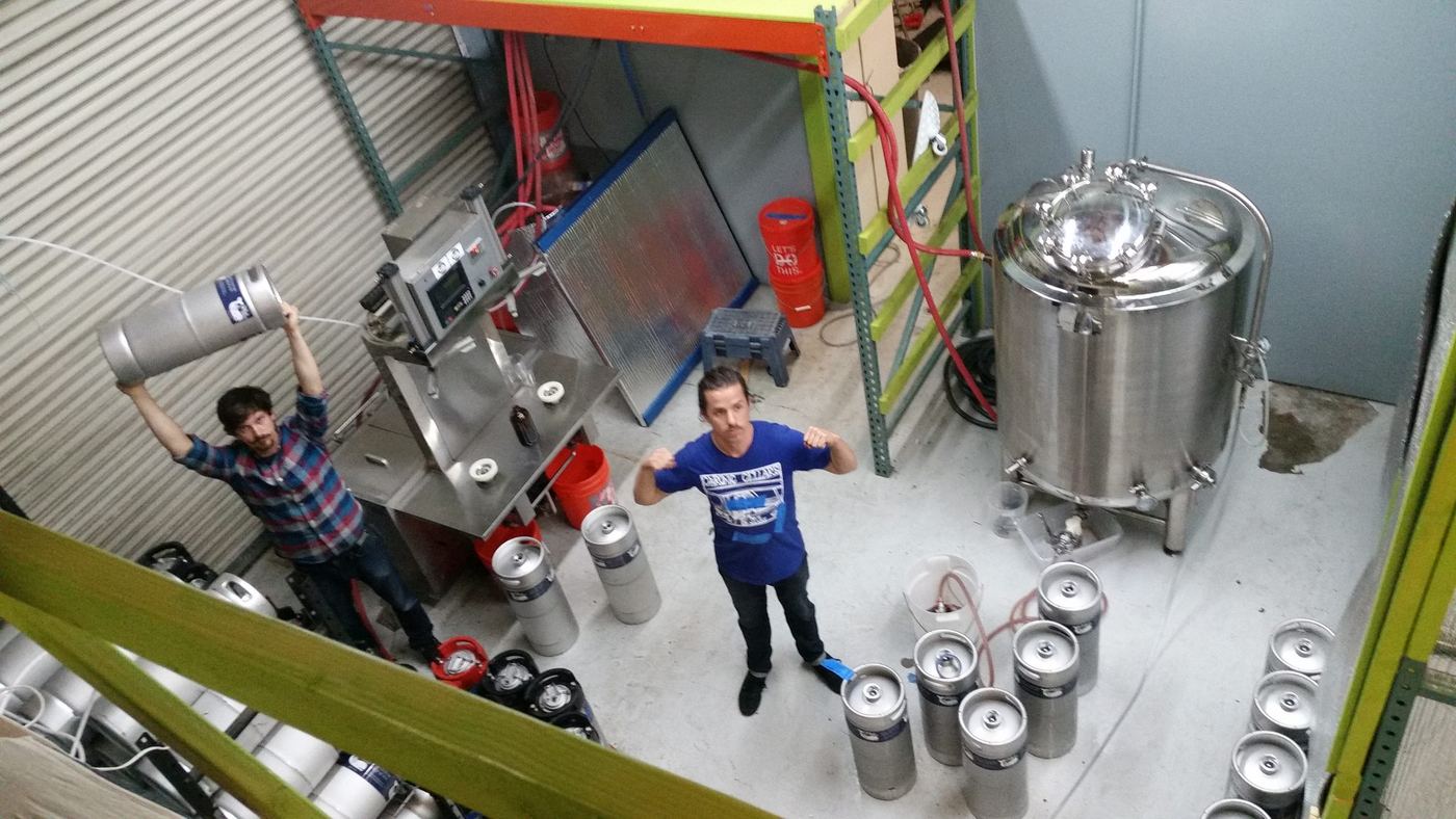 Two of us on the floor early on, one hoisting a keg overhead, next to the keg filler and a small brite tank
