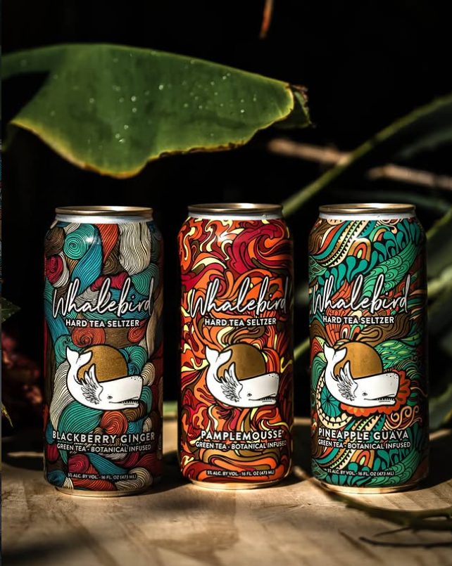 Three Whalebird Hard Tea Seltzer cans staged outdoors under a large leaf