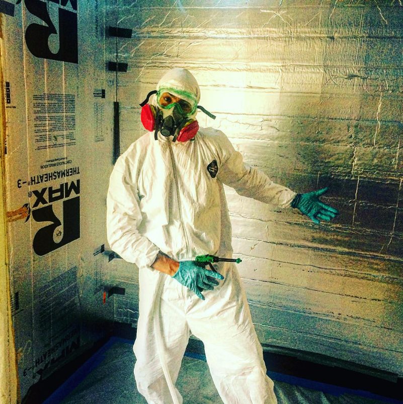 Suited up in a respirator and coveralls to spray foam insulation onto the cold room wall