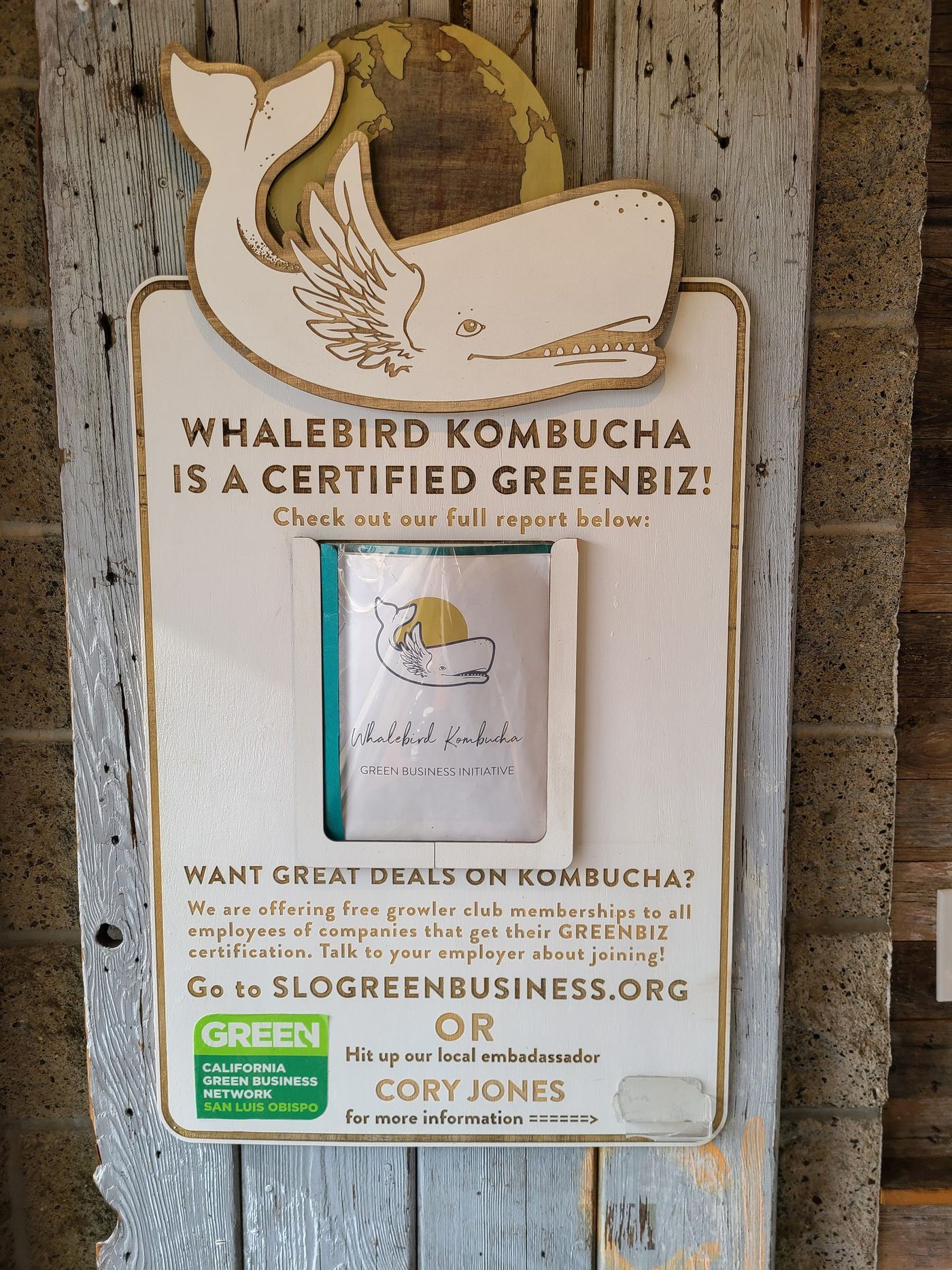 A wall sign announcing Whalebird's certified Green Business status next to a large whale logo cutout