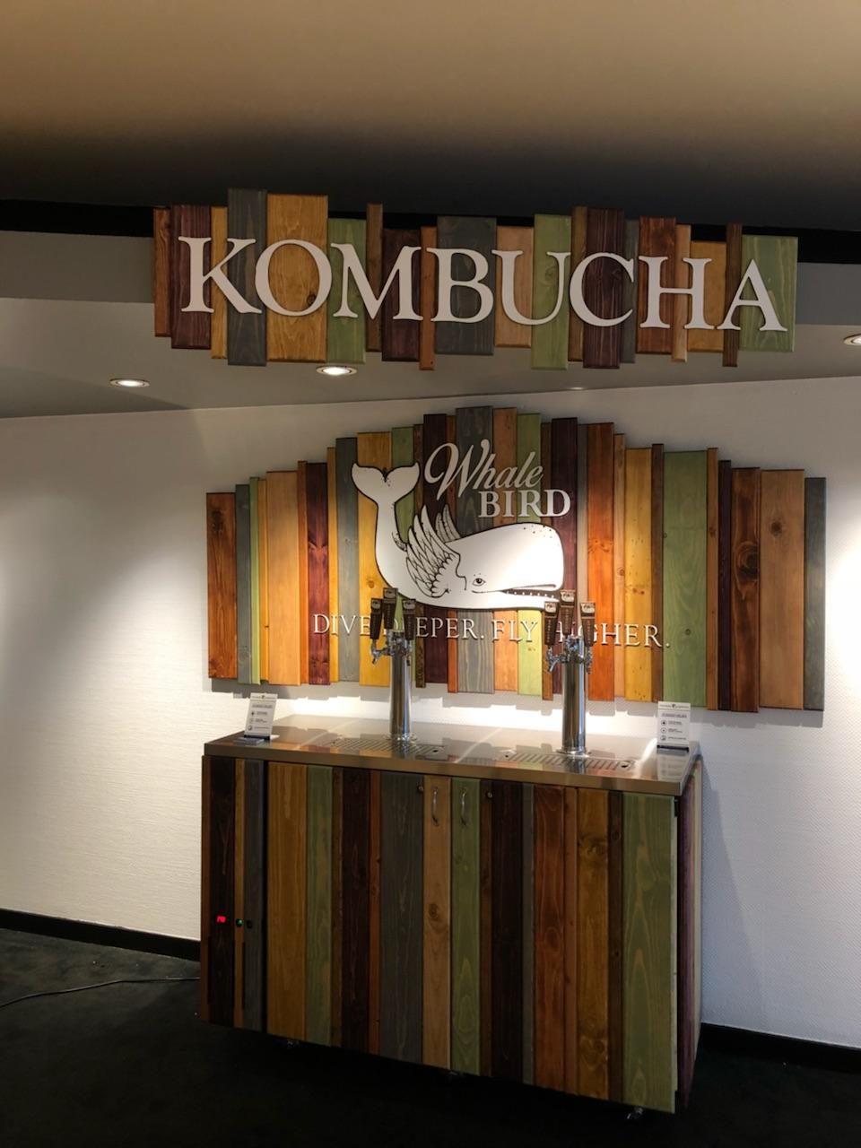 The taproom's reclaimed wood Kombucha sign and Whale Bird logo mounted above a rolling tap cart with two beer towers