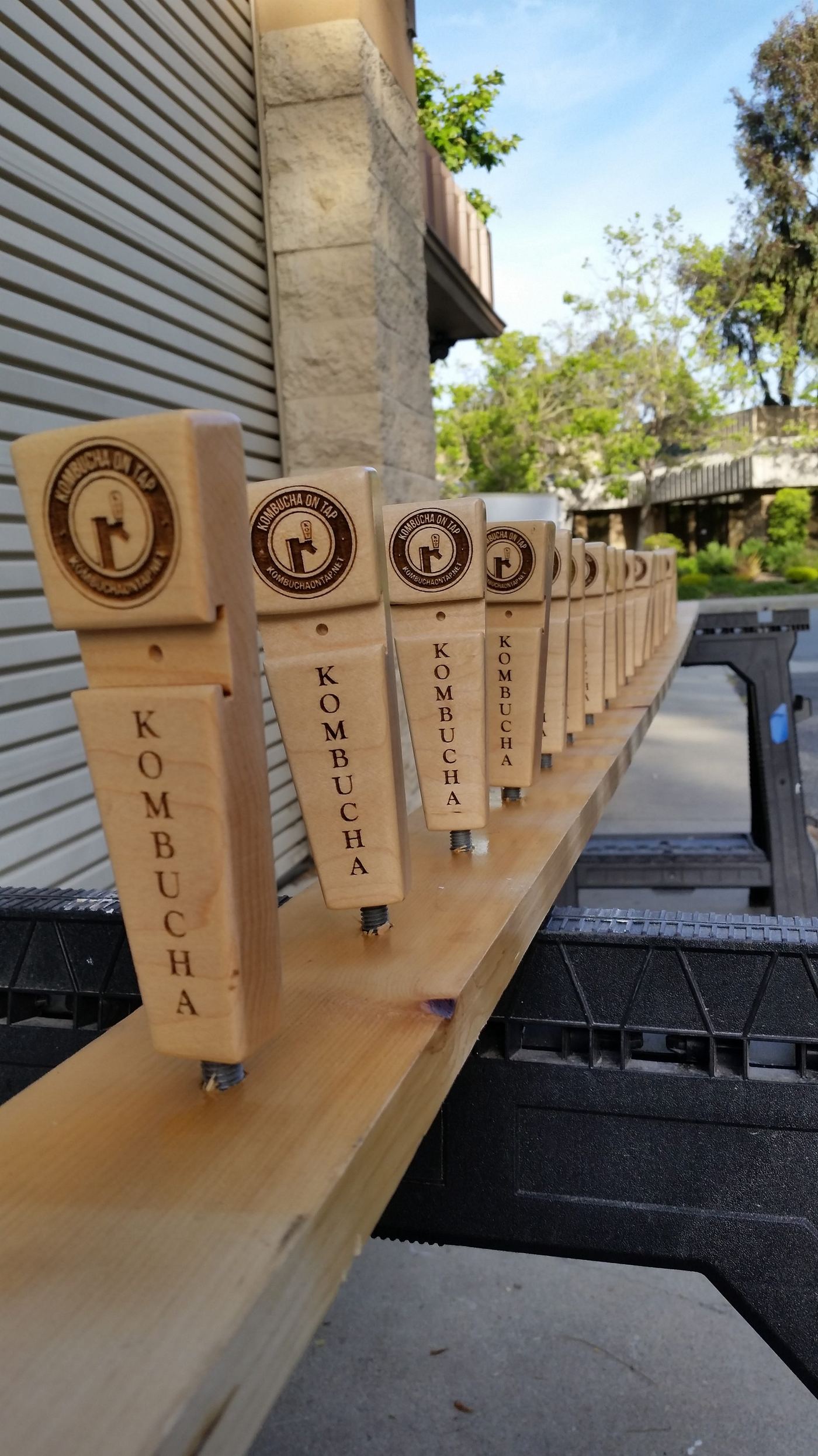 A long row of 'Kombucha on Tap' wood handle blanks laid out for assembly