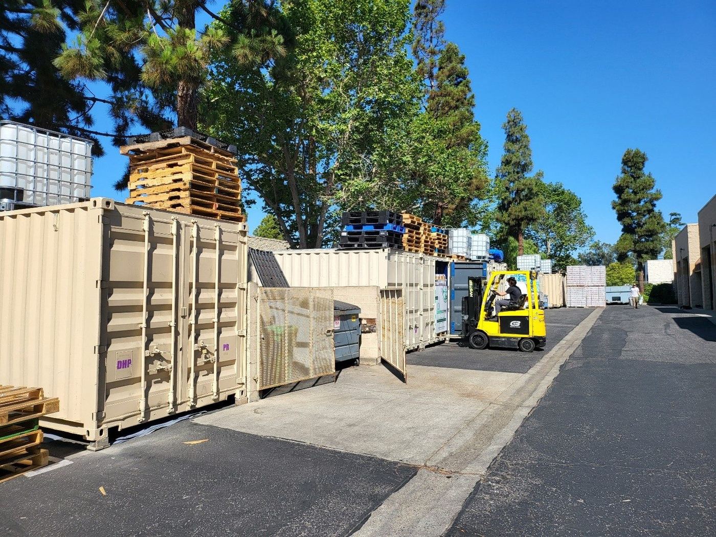 The yard out back, shipping containers and stacked pallets with a forklift working between them