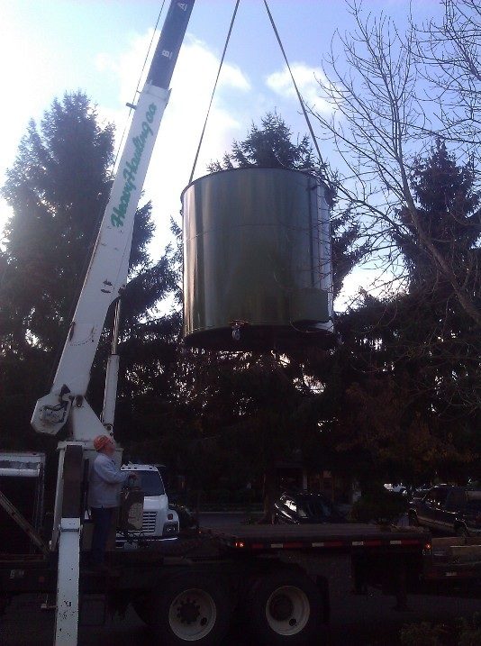 The green digester tank being lifted by crane, trees and sky in the background