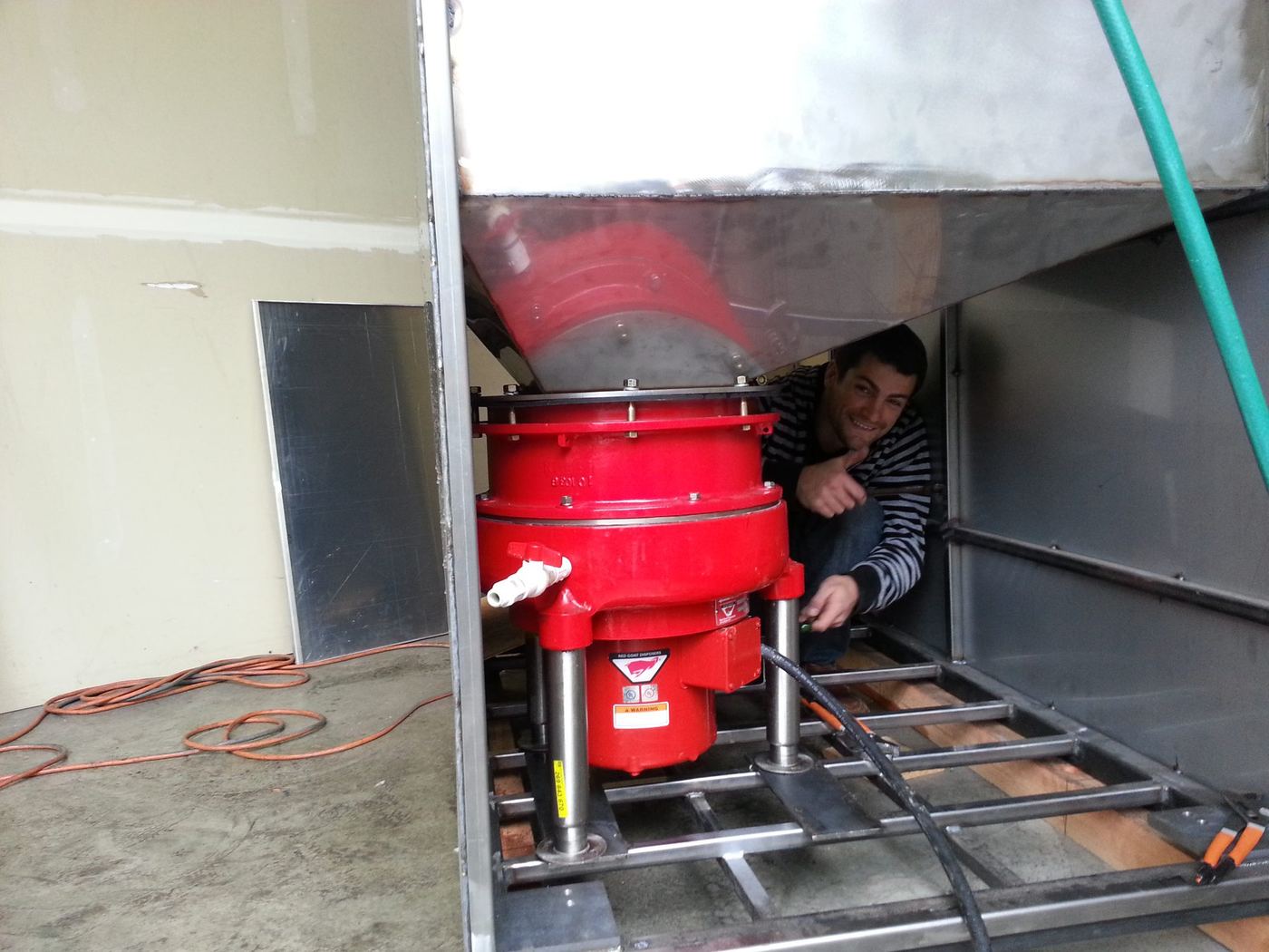 Installing the red grinder assembly underneath the enclosure, crouched in the frame to bolt it in