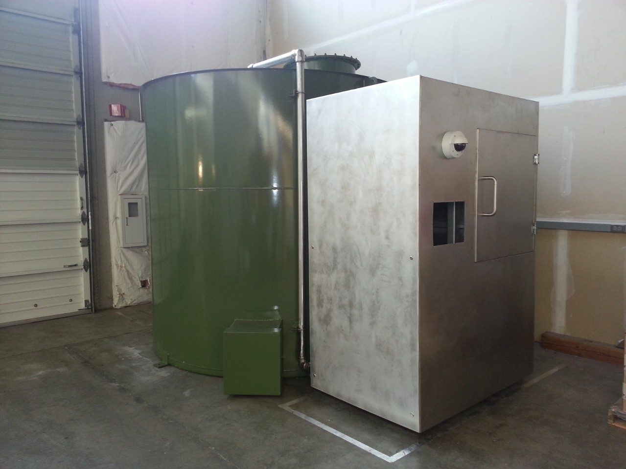 The finished third-generation Harvestor in the shop, green tank and stainless enclosure with a security camera and access window