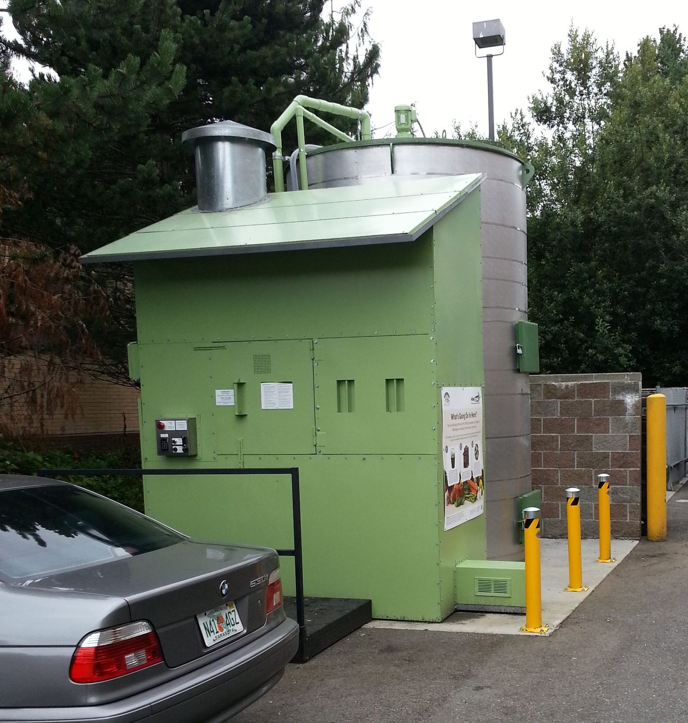 The completed H2O unit installed in a store parking lot, green enclosure and stainless tank next to the dumpster corral it replaced
