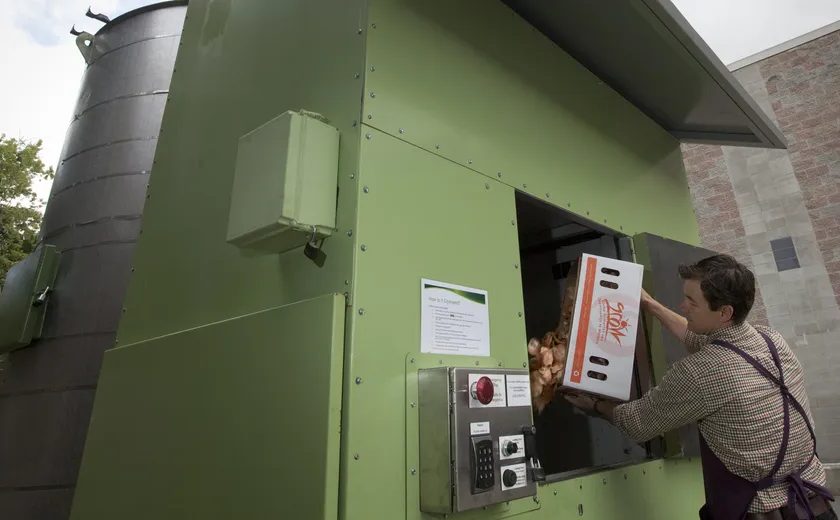 A person loading a box of food waste into the H2O unit's side hatch